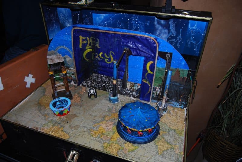 A real flea circus setup in a suitcase, with tiny stage, props, and painted backdrop